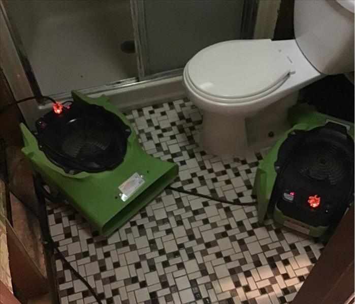 Clean bathroom, flooring, and partially demolished walls with green SERVPRO air movers operating inside the room